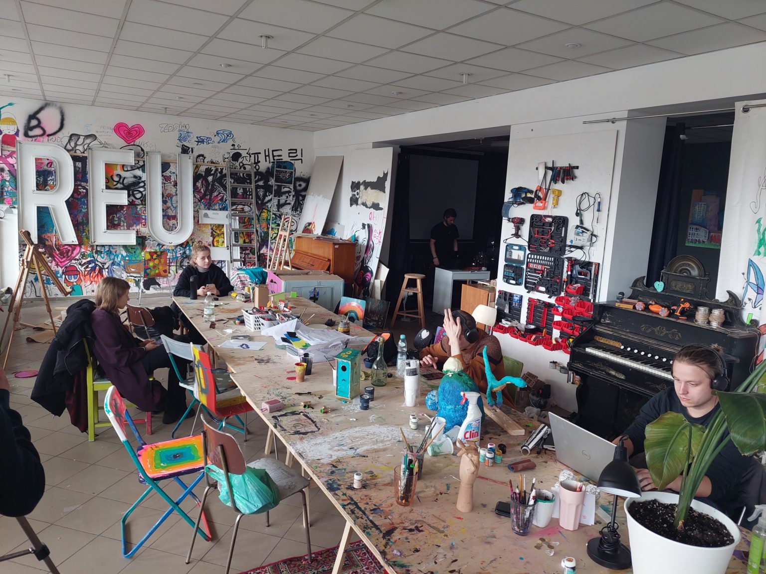 Przy ustawionym na środku pracowni stole kreślarskim siedzą studenci