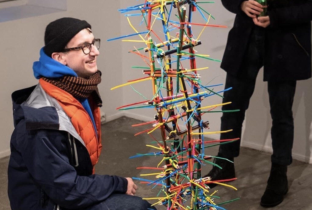 Kacper Tomaszewski kucający obok swojej instalacji w galerii