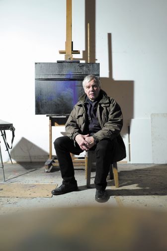 Stanisław Baj w pracowni siedzący na tle swojego obrazu